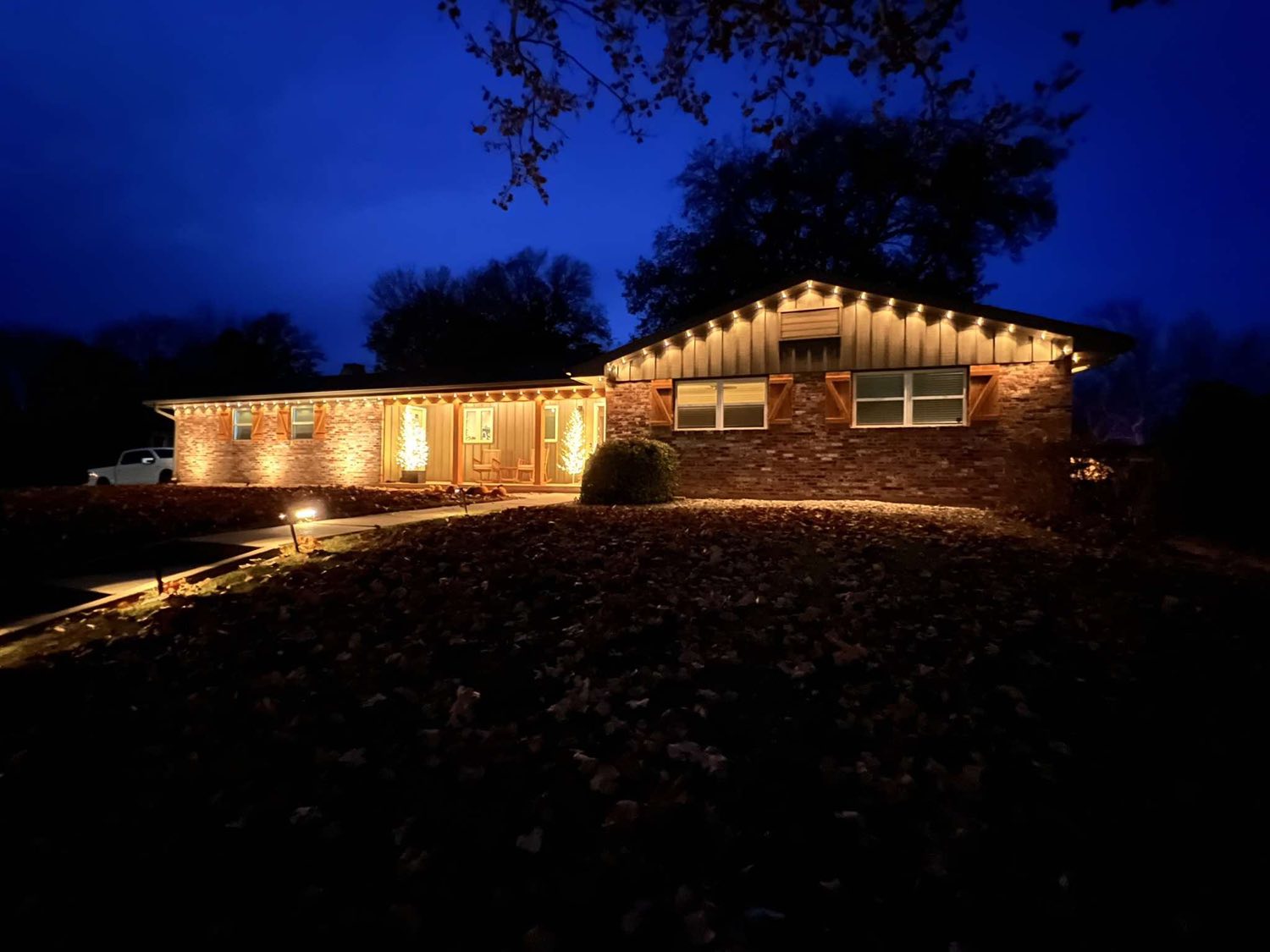 Brick and cedar ranch with warm white Christmas lights and lit porch trees